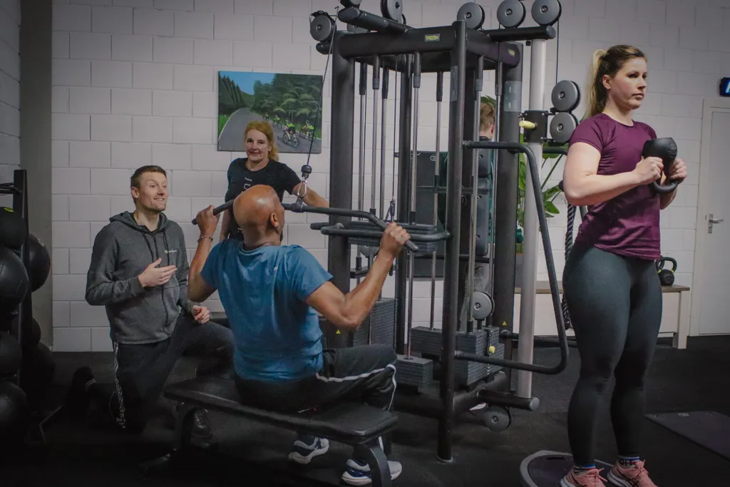 Een trainer moedigt een sporter aan bij het kabelstation, terwijl twee anderen meetrainen in de kleine groep van BerkSports